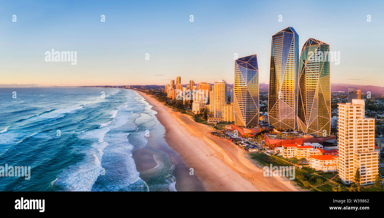 Rising sun shining on modern urban towers of Surfers paradise in Australian Gold Coast facing endless waves of Pacific ocean - aerial panoramic view. Stock Photo