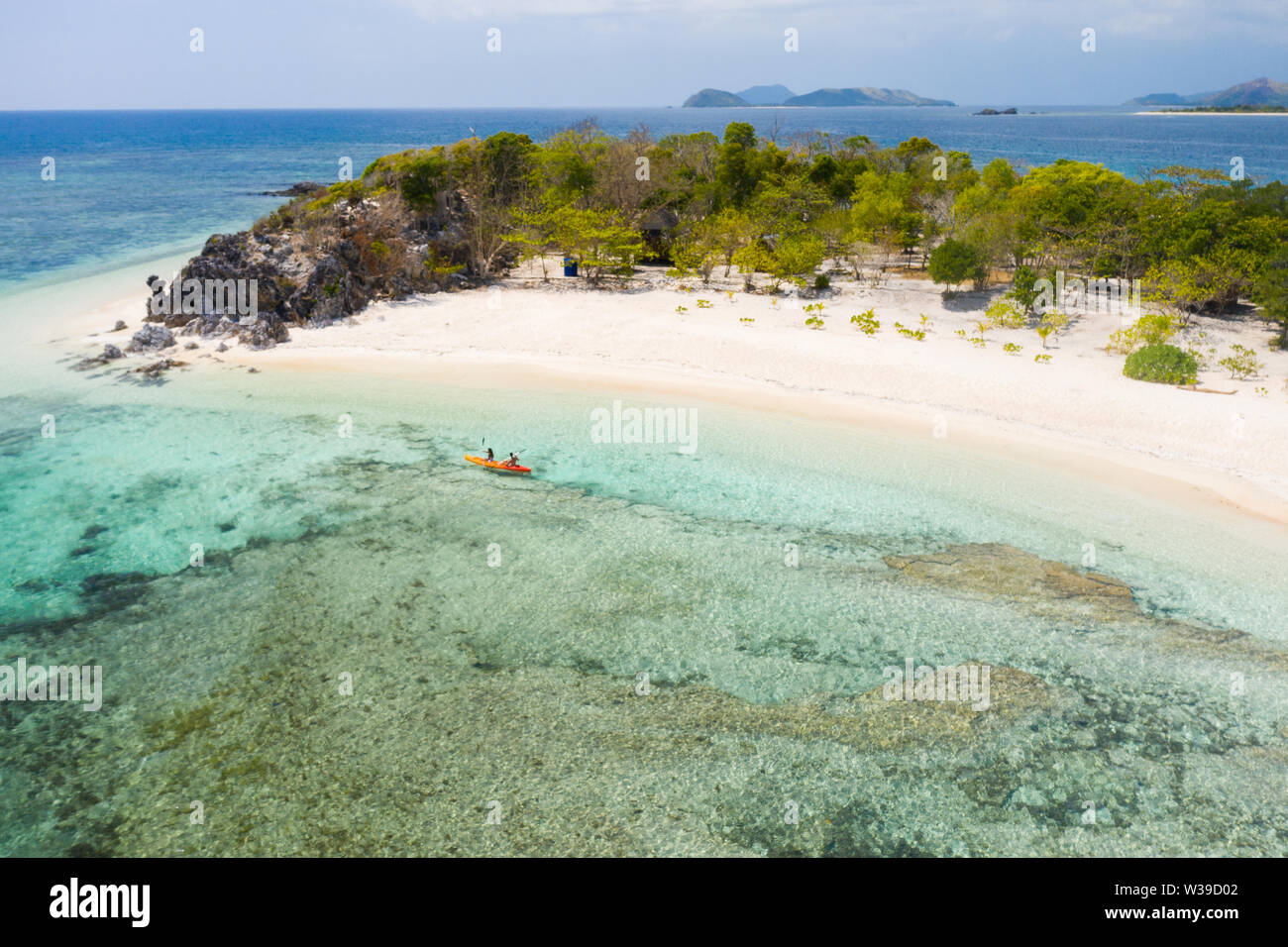 Couple kayaking on a tropical beach with blue water and palm trees ...