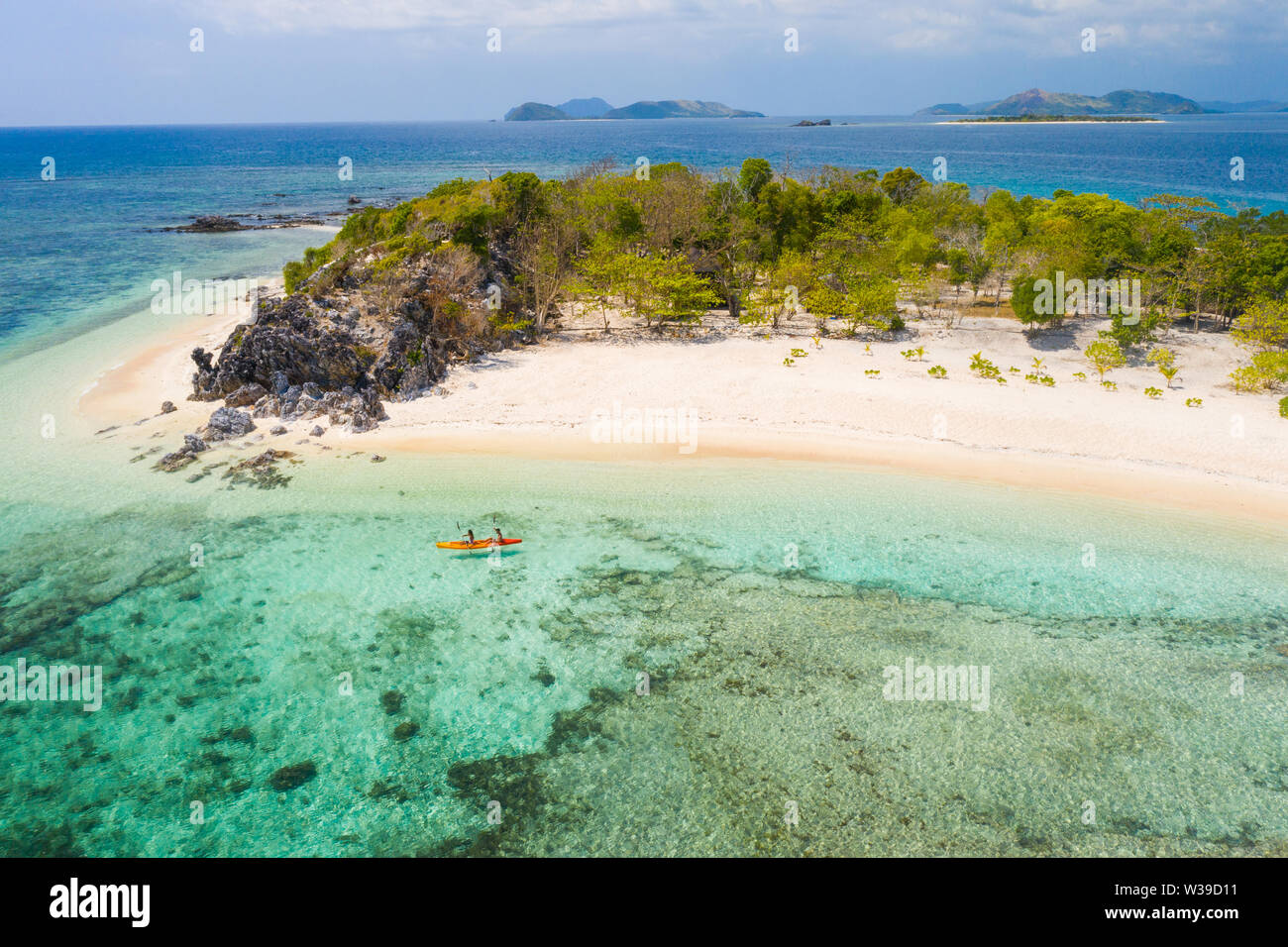 Couple kayaking on a tropical beach with blue water and palm trees ...