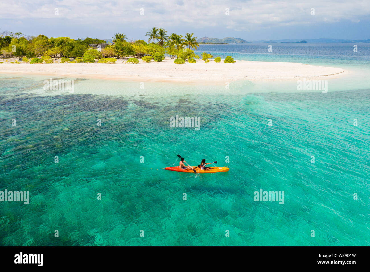 Couple kayaking on a tropical beach with blue water and palm trees ...