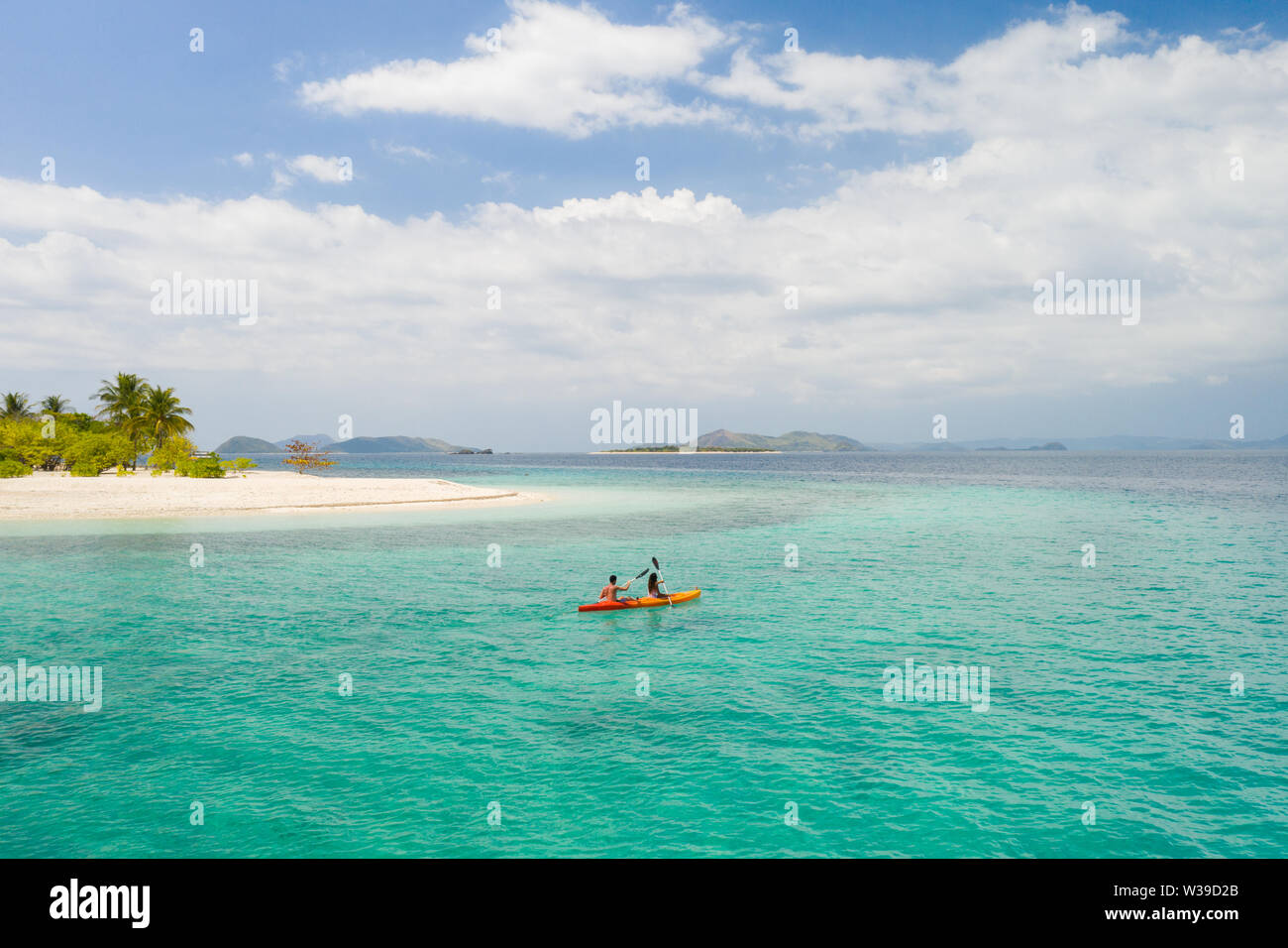 Couple kayaking on a tropical beach with blue water and palm trees ...