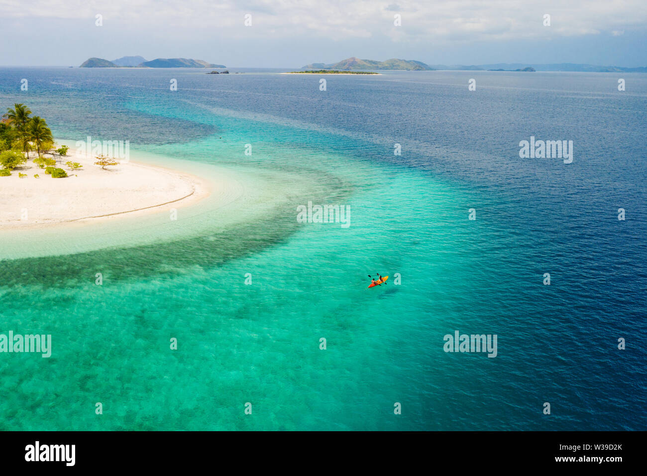 Couple kayaking on a tropical beach with blue water and palm trees ...