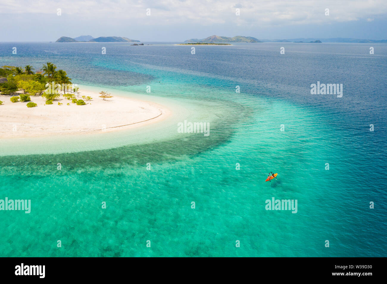 Couple kayaking on a tropical beach with blue water and palm trees ...