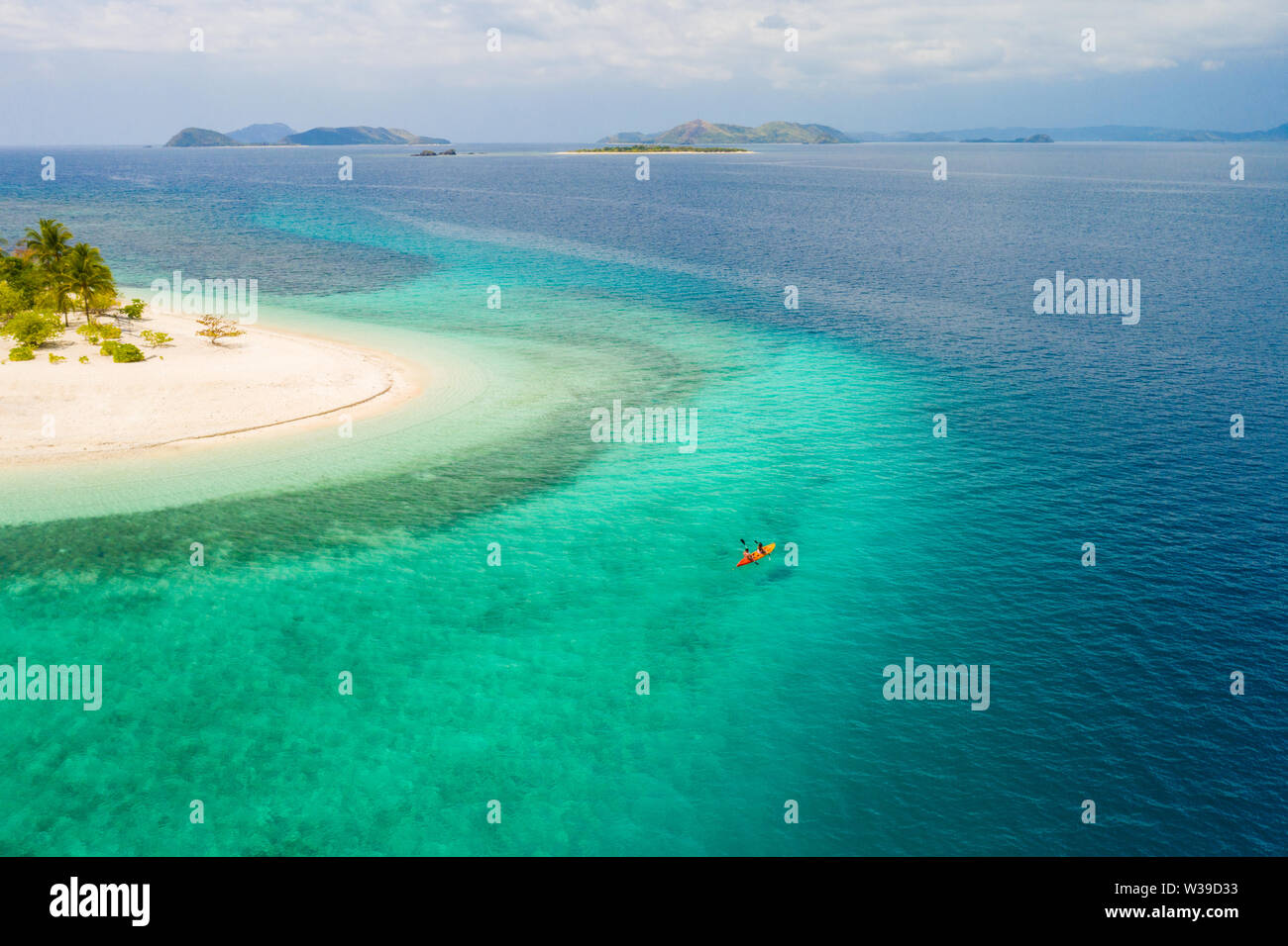Couple kayaking on a tropical beach with blue water and palm trees ...