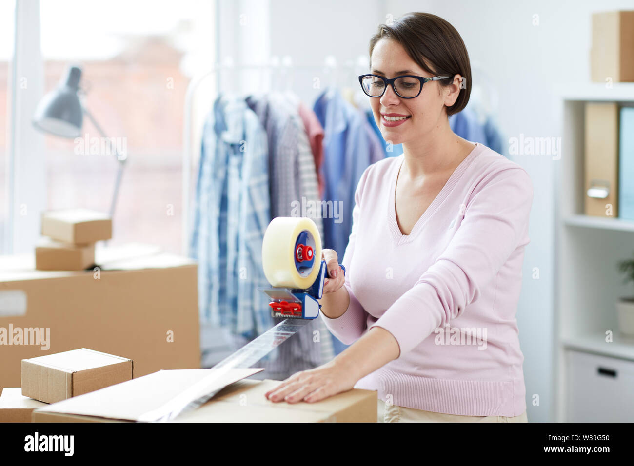 Pretty female with cellotape gun dispenser sealing one of boxes with