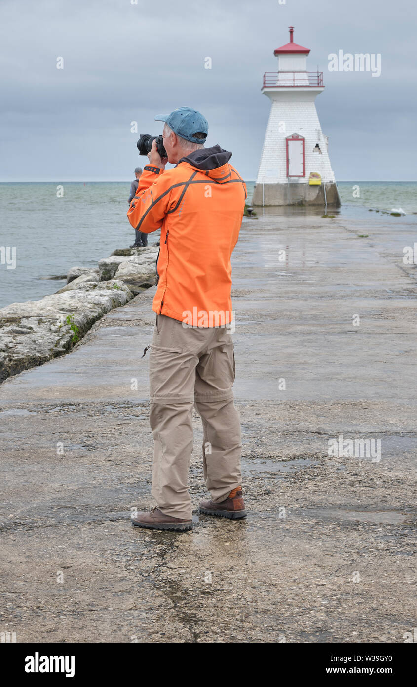 Photographer wearing bright orange jacket takes pictures on a cool dreary and rainy morning near a lighthouse. Stock Photo