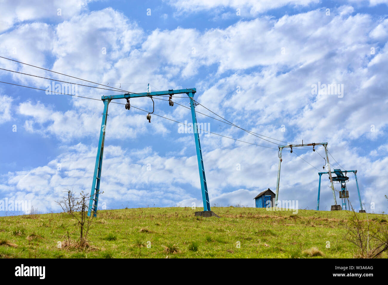 The frame of the mountain cable lift stands apart on the top of the mountain against the background of a deep blue sky with white clouds in the Carpat Stock Photo