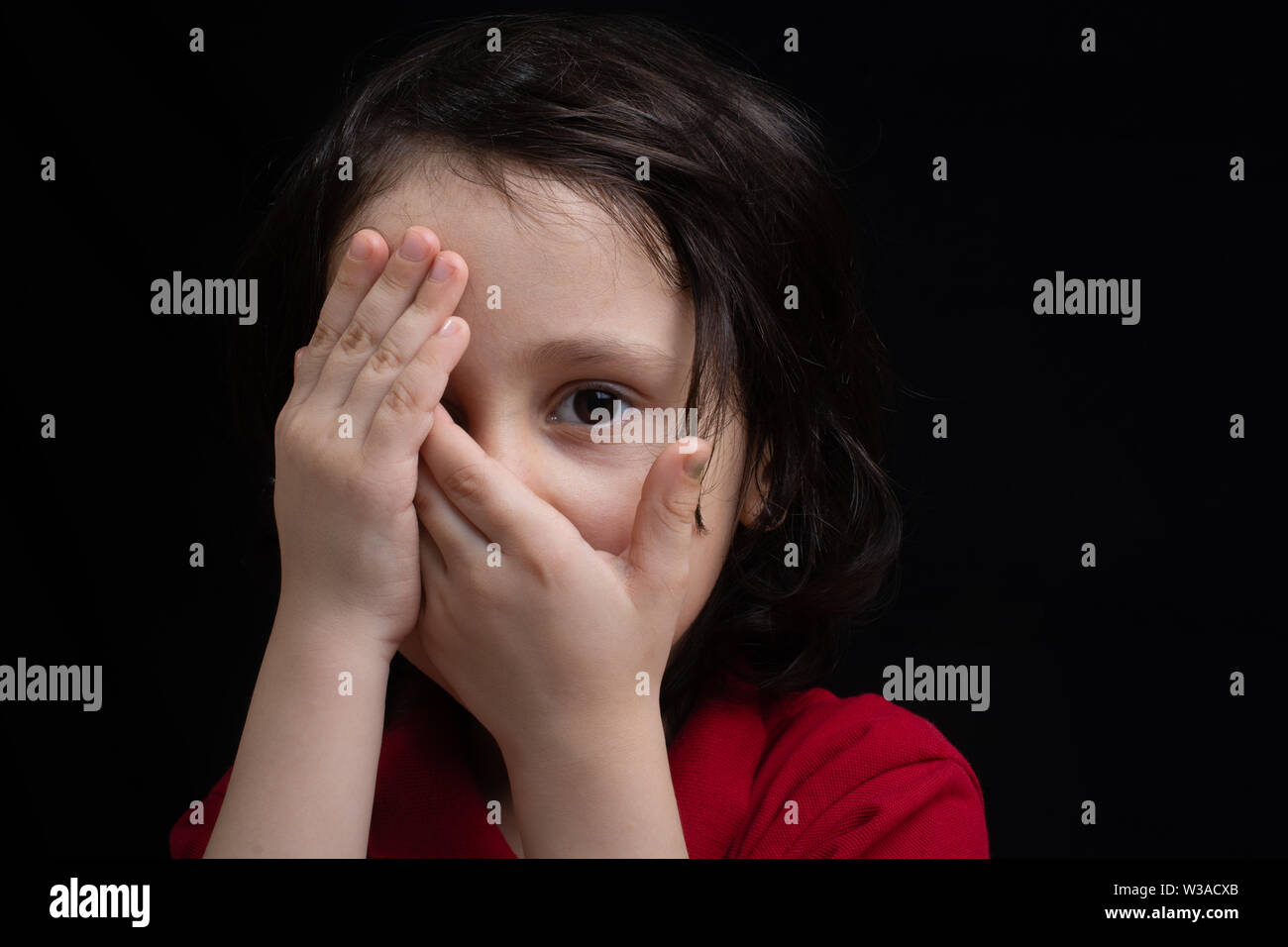 Little boy peeking through one eye covering face and eye with hand ...