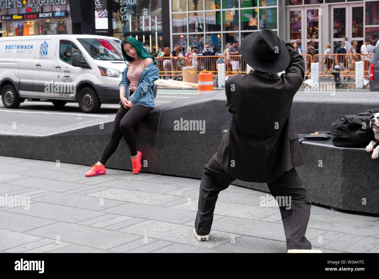 A photographer in a zoot suit and fedora takes a photo of a beautiful Asian woman with green hair. In Times Square, Manhattan, New York City. Stock Photo