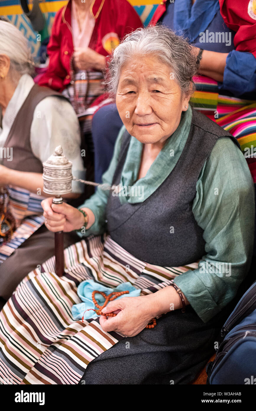 An older woman, likely Nepalese,  prays while holding a Buddhist Prayer wheel. At the Sherpa Kyidug temple in Elmhurst, Queens, New York City. Stock Photo