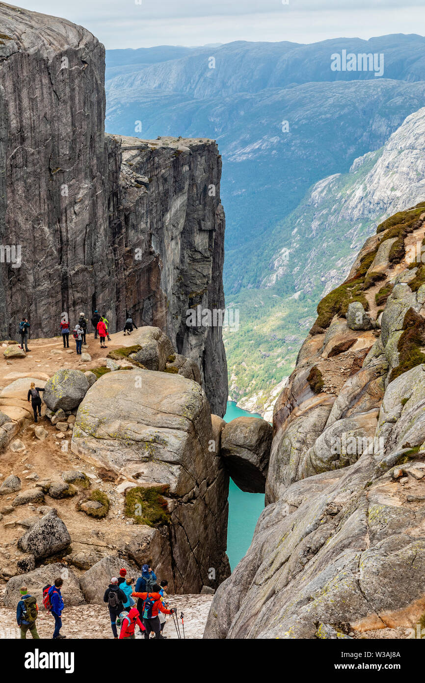 Kjeragbolten, view from the top to the stone stuck between two rocks with fjord in the background and tourists gathered around, Lysefjord, Norway Stock Photo