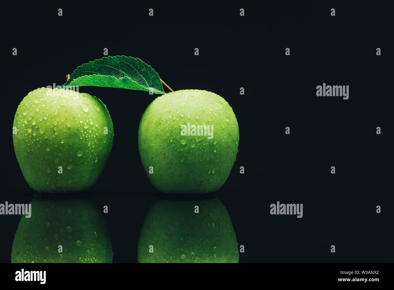 Two green apples on a black glass table background. Stock Photo