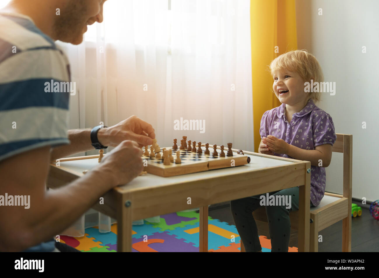 father and daughter having fun together learning to play chess at home Stock Photo