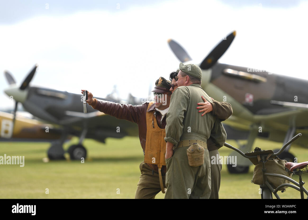Re-enactors in Second World War dress take a selfie in front of Supermarine Spitfire's during the Flying Legends Air Show at IWM Duxford. Stock Photo