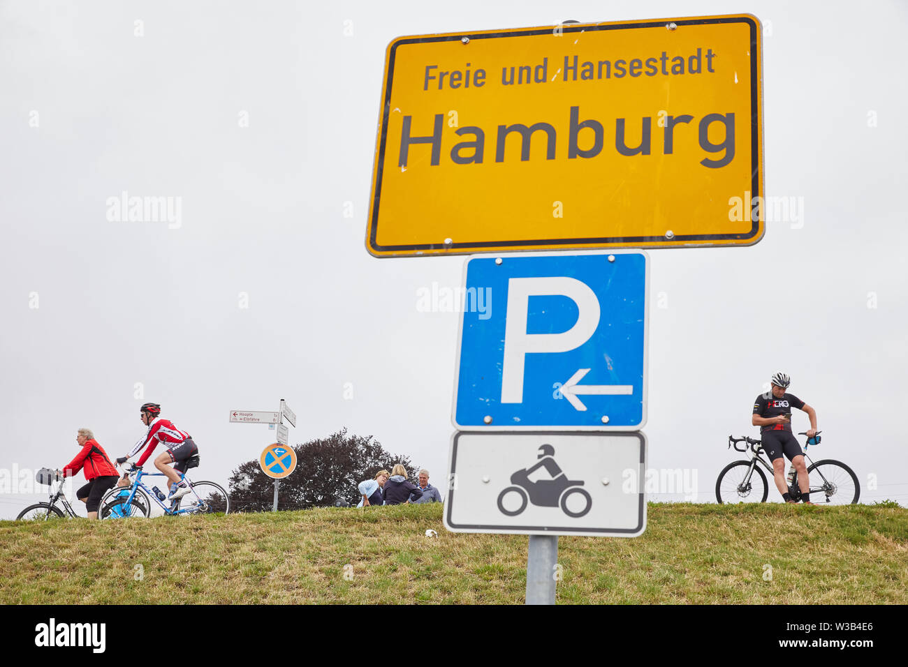 14 July 2019, Hamburg: Behind a town sign with the inscription: 'Freie und Hansestadt Hamburg' cyclists pass pedestrians on the Zollenspieker main dike. Photo: Georg Wendt/dpa Stock Photo