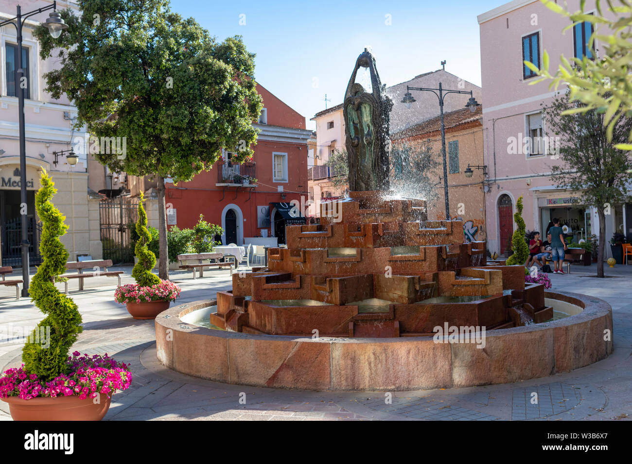 OLBIA, ITALY - June 12, 2019: Moody square in the old town, with fountain, statue and flower decoration, surrounded by cafes. Stock Photo