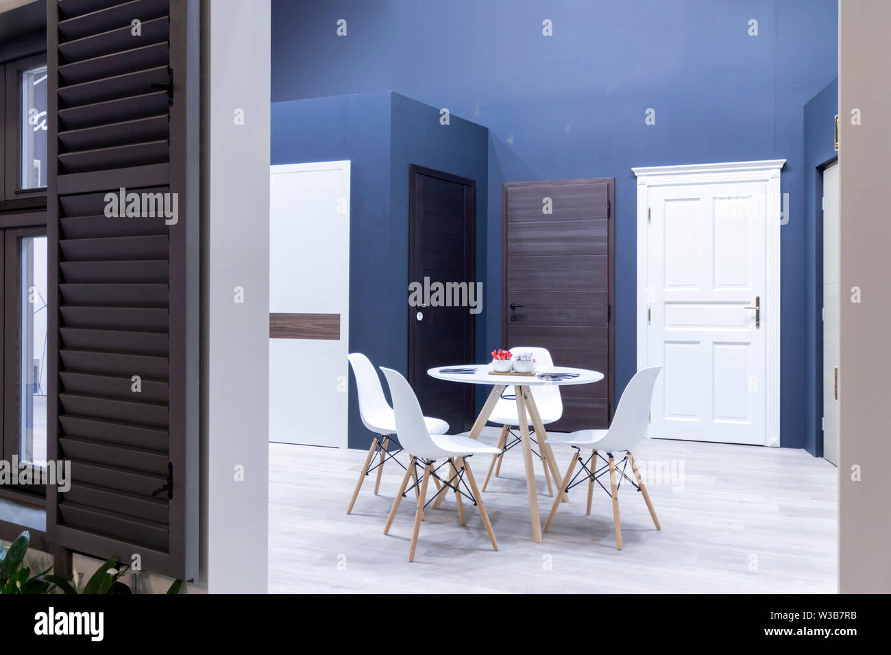 A collection of doors on display in a home depot. White floor, table with four chairs and decoration. Stock Photo