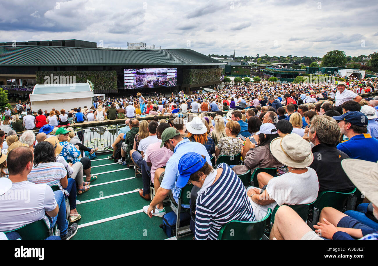 London, UK, 14th July 2019: Spectators on Murray Mount (Henman Hill) watch a big screen showing Novak Djokovic playing against swiss Roger Federer during their men's final match on the 13th day of the 2019 Wimbledon Championships at The All England Lawn Tennis Club in Wimbledon, southwest London. Credit: Frank Molter/Alamy Live news Stock Photo