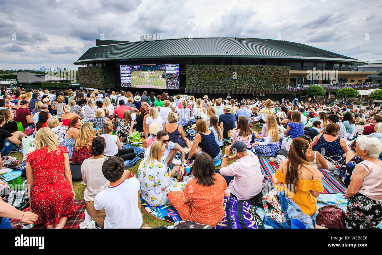 London, UK, 14th July 2019: Spectators on Murray Mount (Henman Hill) watch a big screen showing Novak Djokovic playing against swiss Roger Federer during their men's final match on the 13th day of the 2019 Wimbledon Championships at The All England Lawn Tennis Club in Wimbledon, southwest London. Credit: Frank Molter/Alamy Live news Stock Photo