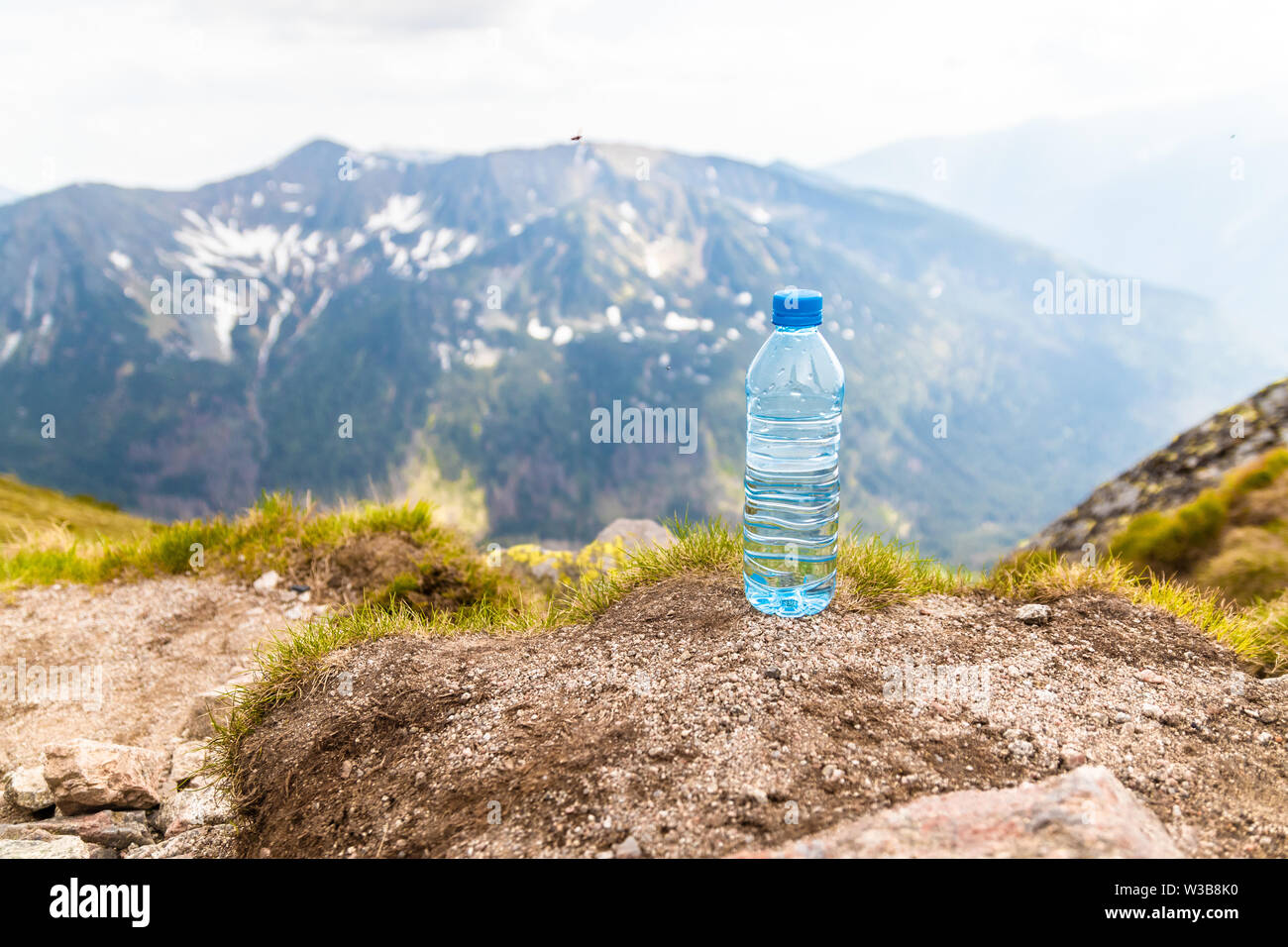 Plastic bottle with fresh drinking water stands on a stone high in the mountains on a sunny day. Stock Photo