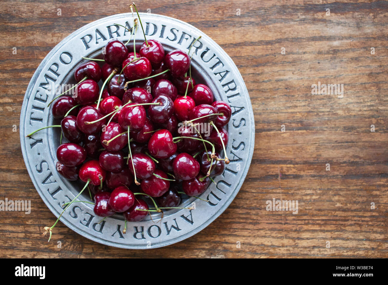 Sweet cherries (Prunus avium) sit in a silver bowl with the Spanish phrase  meaning, "Health, love, money and the time to enjoy them Stock Photo - Alamy