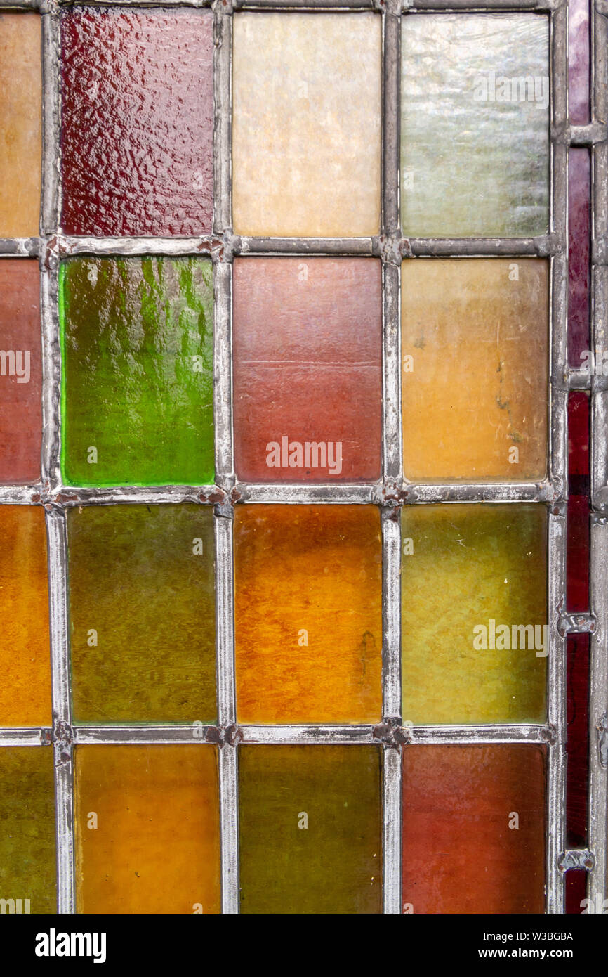 Detail of a stained glass window, glass coloured red, green, yellow, and orange, with lead