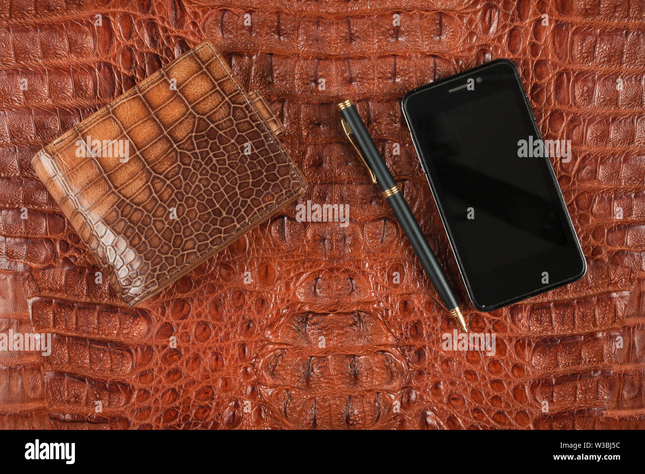 Men's wallet, phone and pen lies on genuine crocodile leather. View from above. Stock Photo