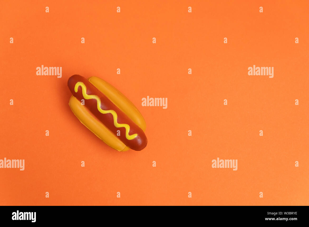 Artificial plastic hot dog on orange background with copy space