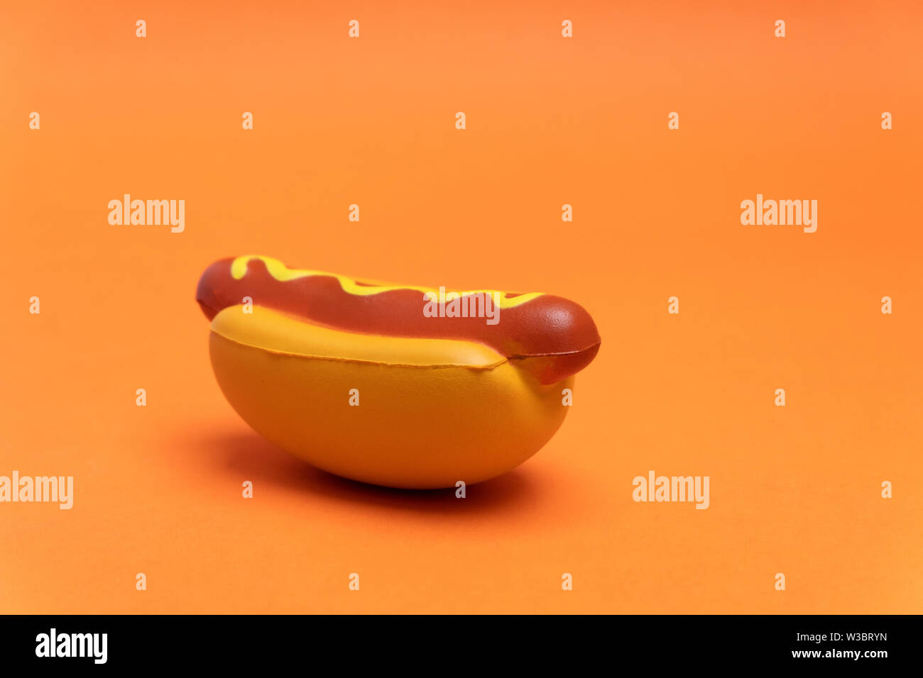 Artificial plastic hot dog on orange background with copy space