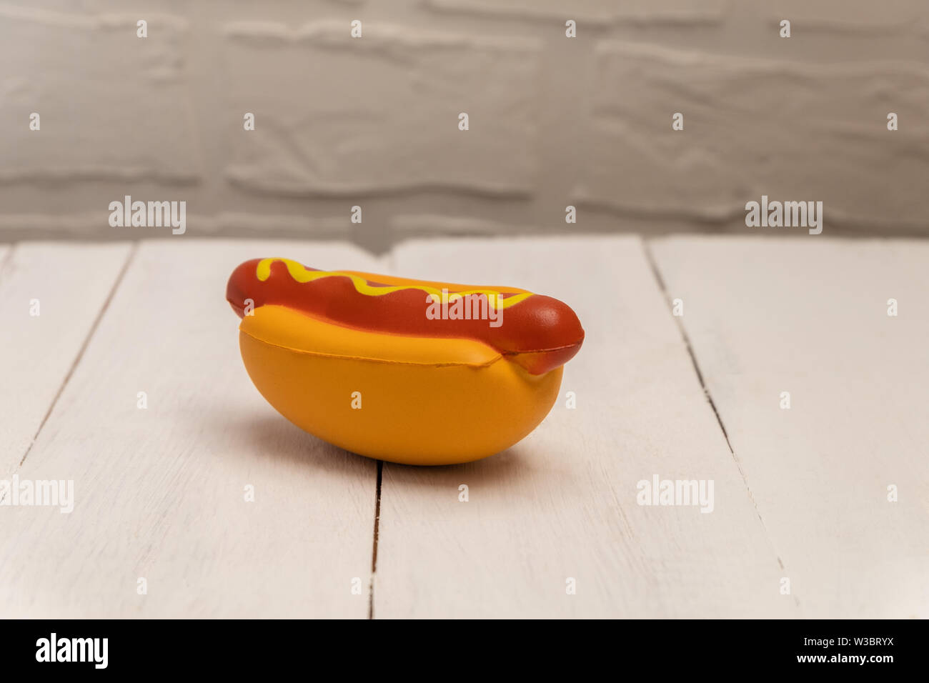 Artificial plastic hot dog toy on white wooden background with copy