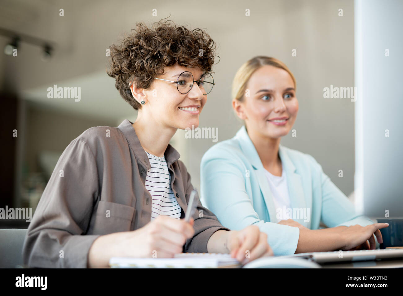 Two happy female colleagues looking at data on computer screen Stock Photo