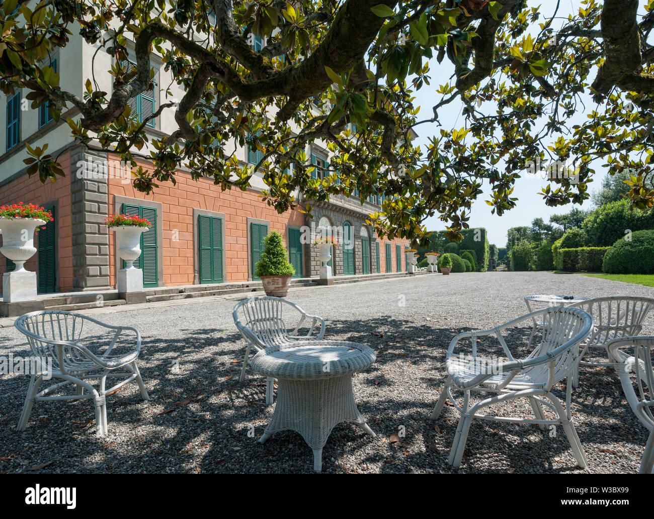 Marlia, Lucca, Italy - 2018, May 25: Tables and chairs in the shadow of a large tree, in the villa's forecourt. Villa Reale in Marlia, Lucca, Italy. Stock Photo