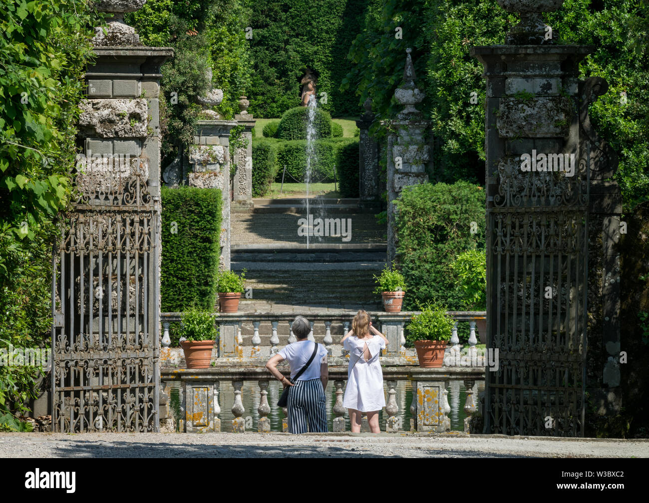 Marlia, Lucca, Italy - 2018, May 25: A glimps of the park of Villa Reale. An old iron gate opens to the formal garden. Tourists admire and take pictur Stock Photo