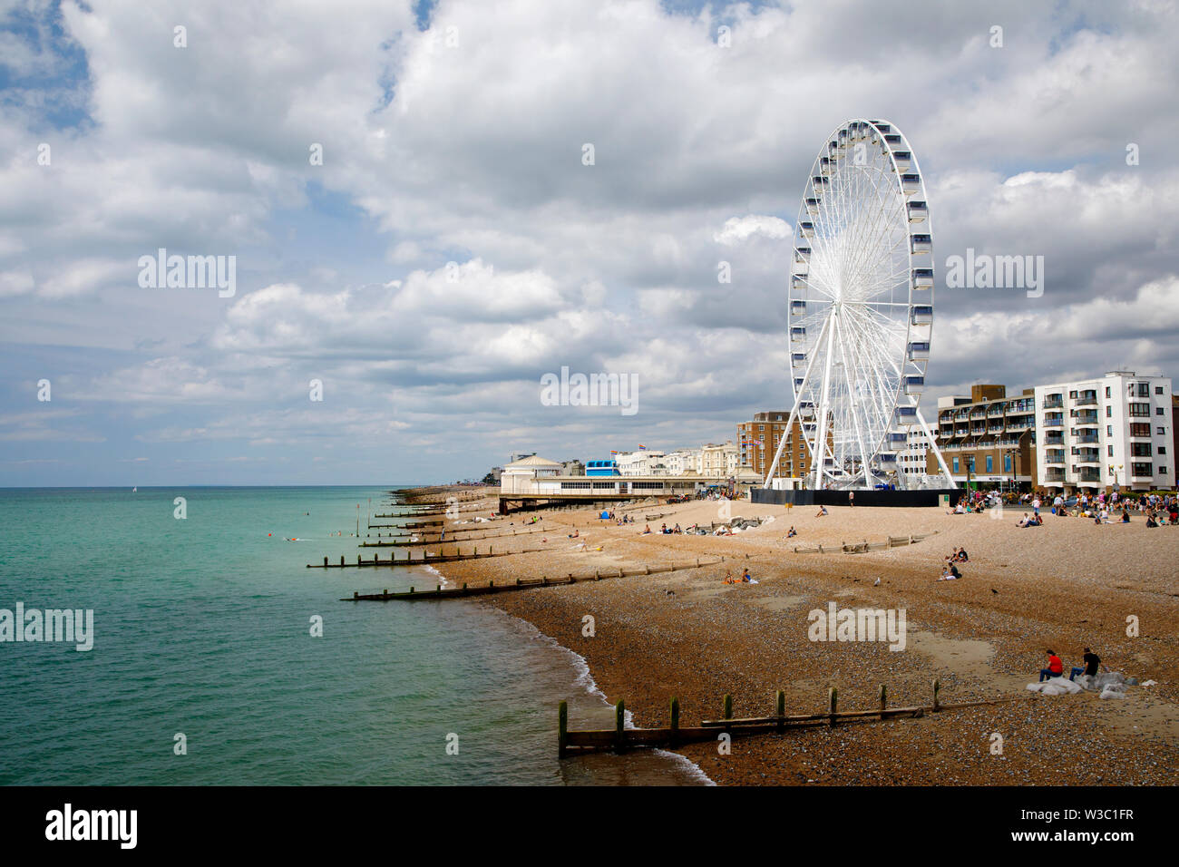 WORTHING, UK - JULY 13, 2019: People enjoy a day out on the pebble beach in Worthing with newly opened Wheel Stock Photo