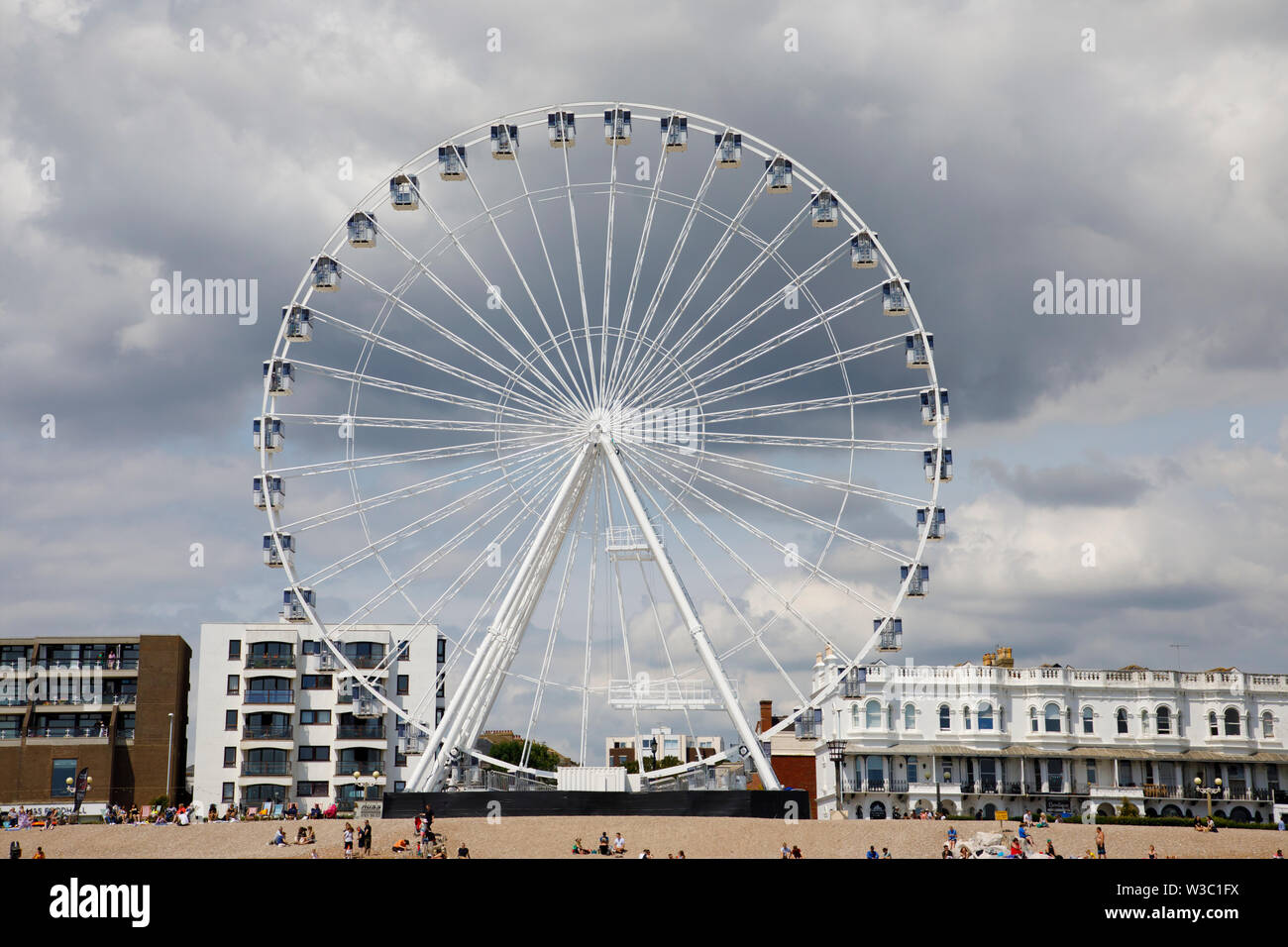 WORTHING, UK - JULY 13, 2019: People enjoy a day out on the pebble beach in Worthing with newly opened Wheel Stock Photo