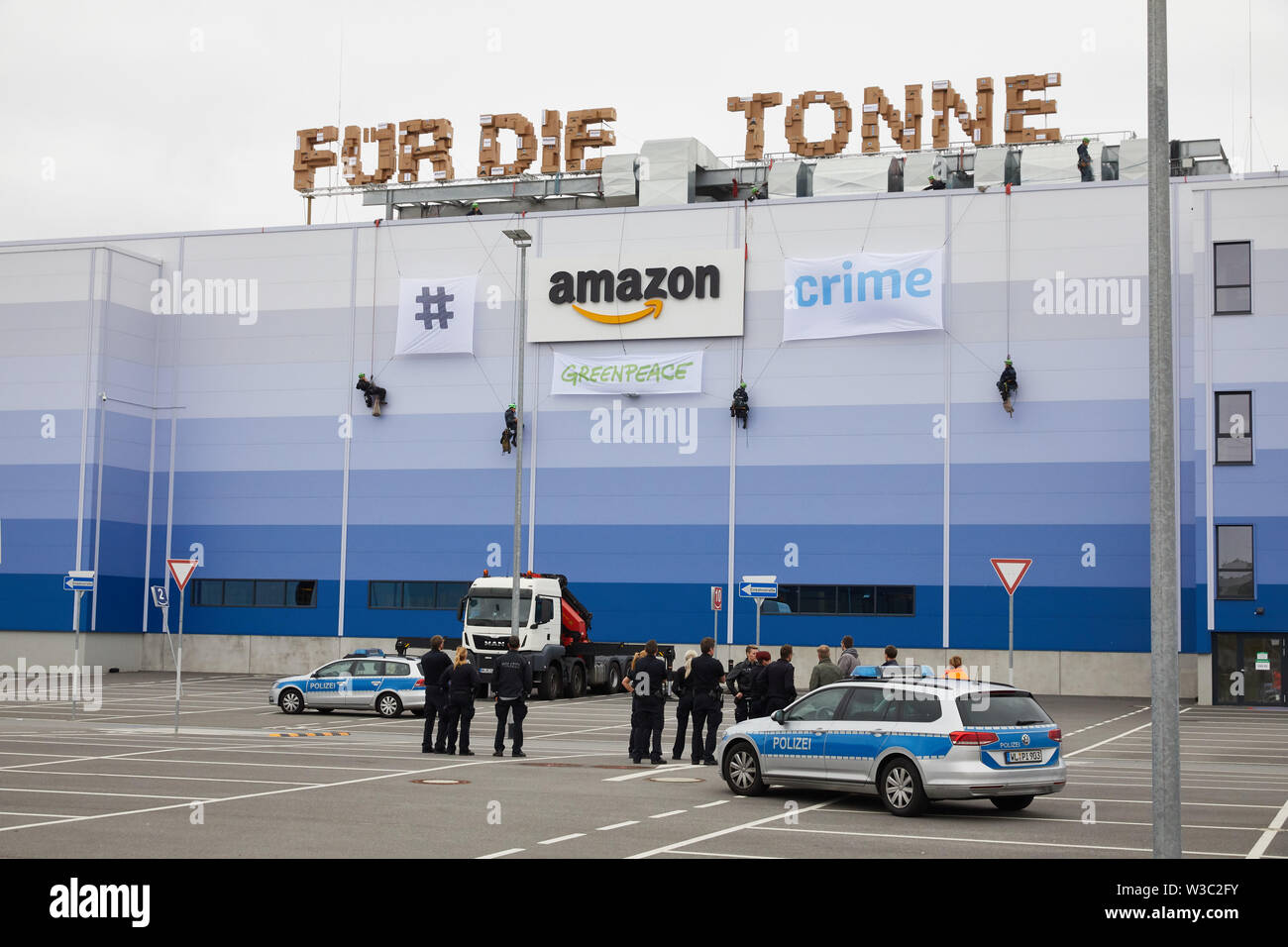 Winsen, Germany. 14th July 2019. Greenpeace activists abseil down the Amazon  Logistik Winsen GmbH building. The activists had climbed onto the building  and had erected a 27-metre-long lettering "Für die Tonne" from