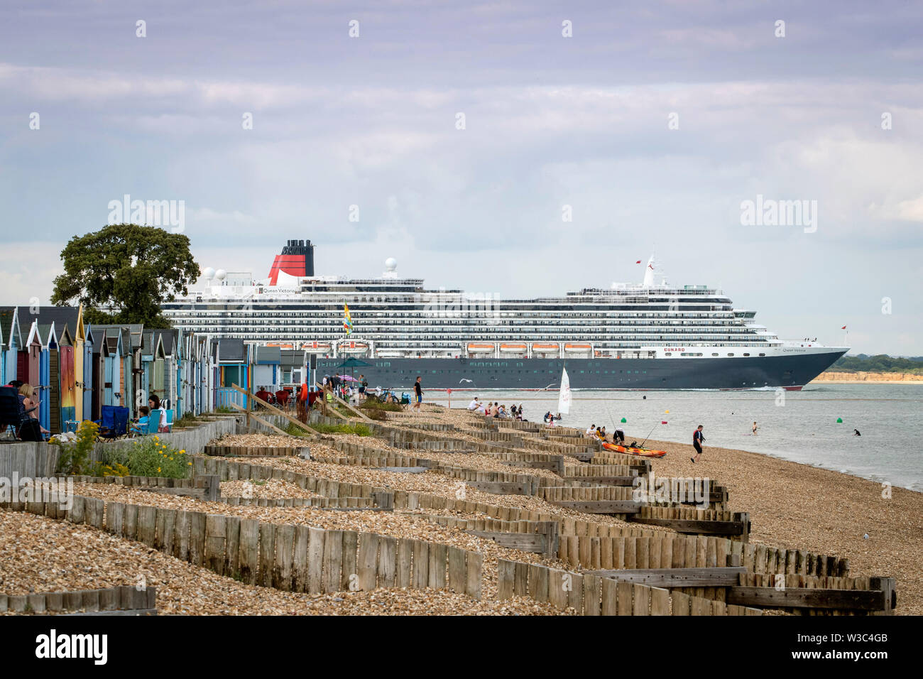 Southampton, Hampshire, UK. 14th July 2019. UK Weather: Beachgoers enjoy a hot summer's evening at Calshot beach in Southampton as cruise ship Queen Victoria passes by. Credit: Stuart Martin/Alamy Live News Stock Photo