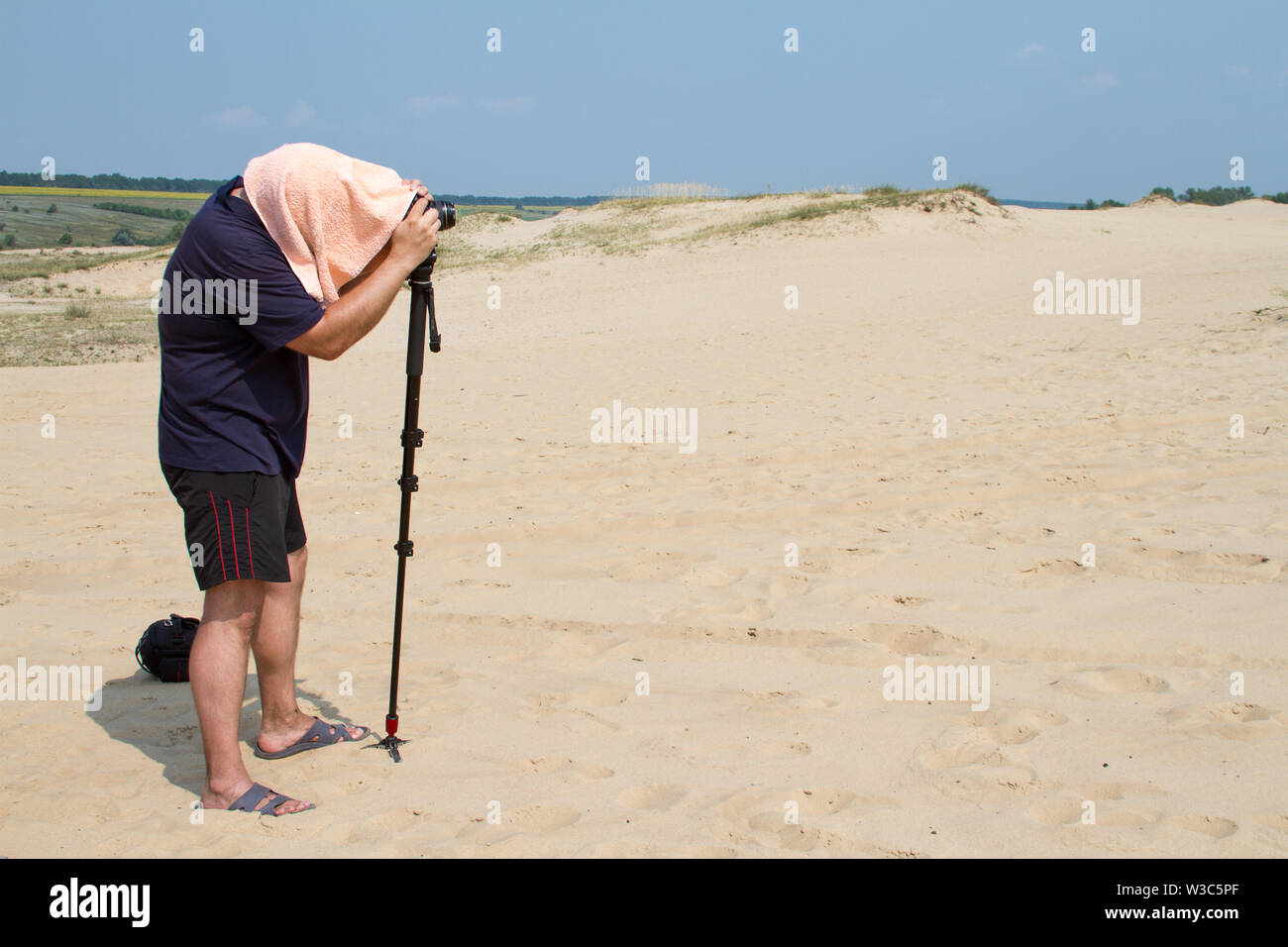 Kharkiv, Ukraine - July 31, 2016: Adult male photographer with a towel on his head from the heat is taking pictures with a camera on a stand in the de Stock Photo