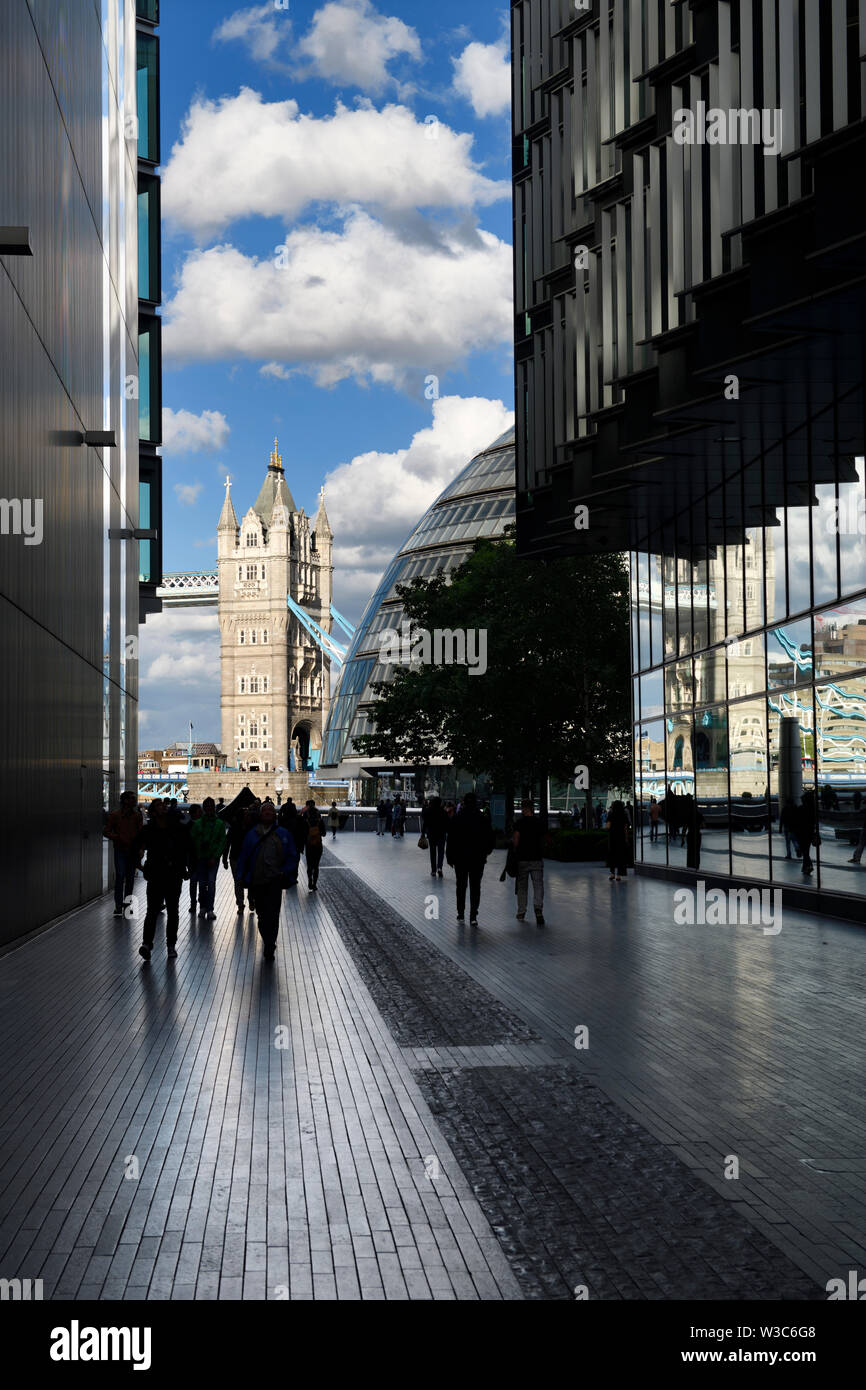Shiny granite pavers with pedestrians on More London Riverside pedestrian walkway with reflections in glass buildings of Tower Bridge London England Stock Photo