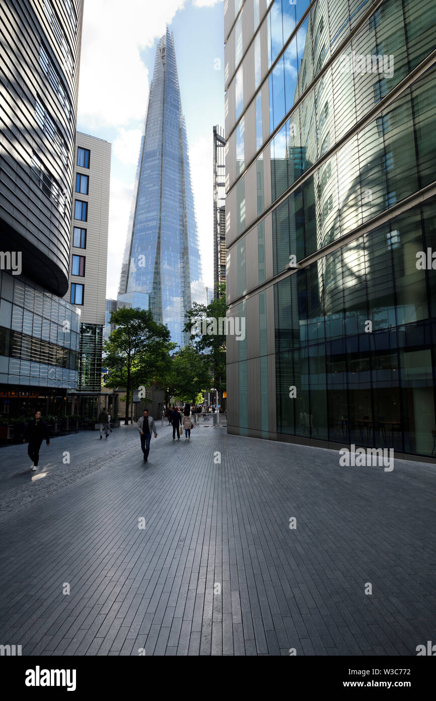 Glass spire of The Shard against a bright sky and shiny granite pavers on More London Riverside pedestrian walkway London England Stock Photo