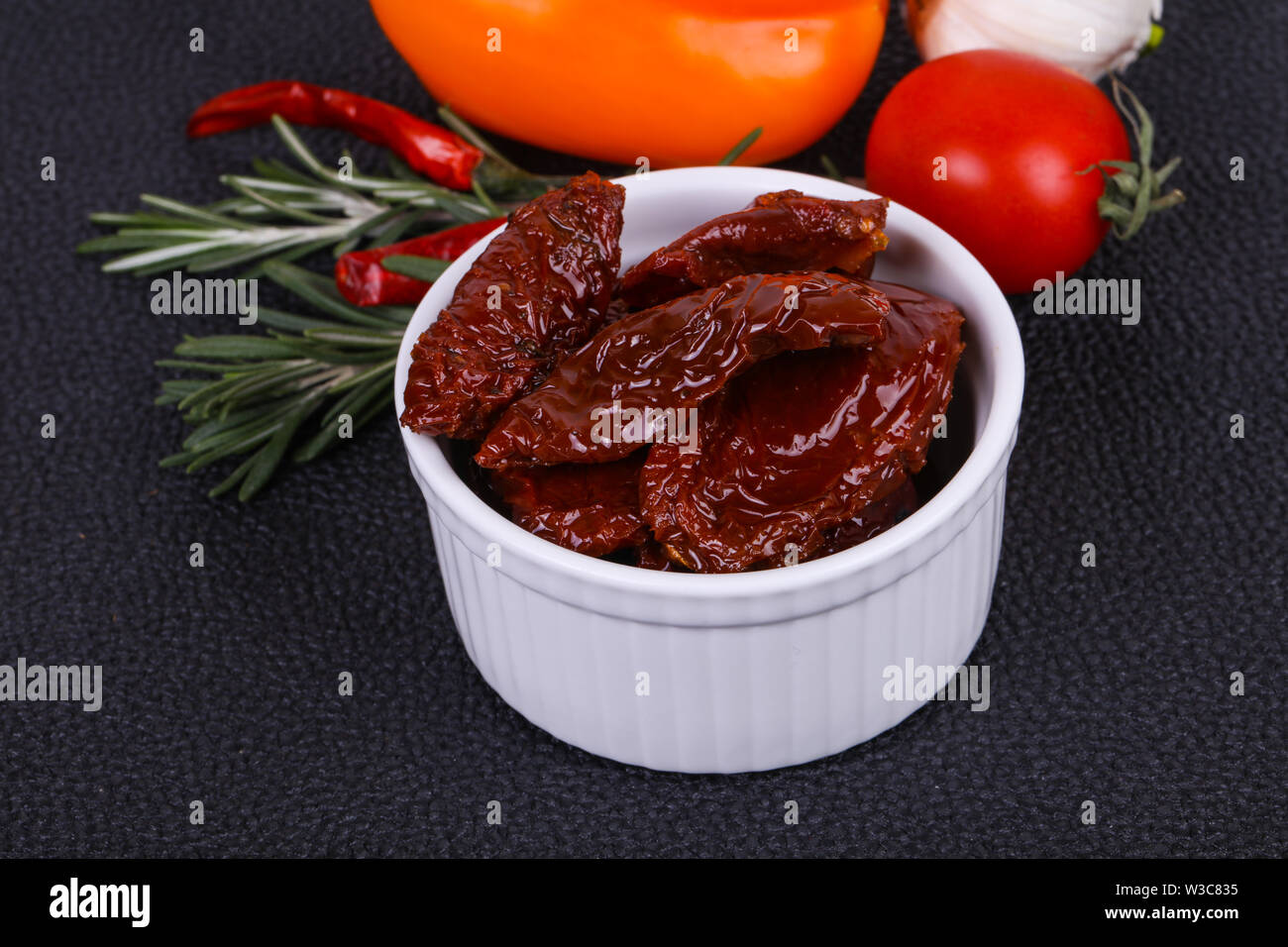 Dried tomatoes in the bowl with olive oil served rosemary, salad leaves
