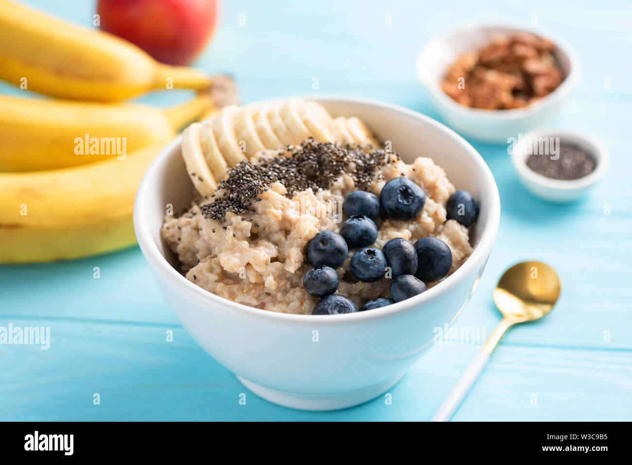 Oatmeal porridge with banana, blueberries and chia seeds in white bowl on blue background. Healthy breakfast food Stock Photo