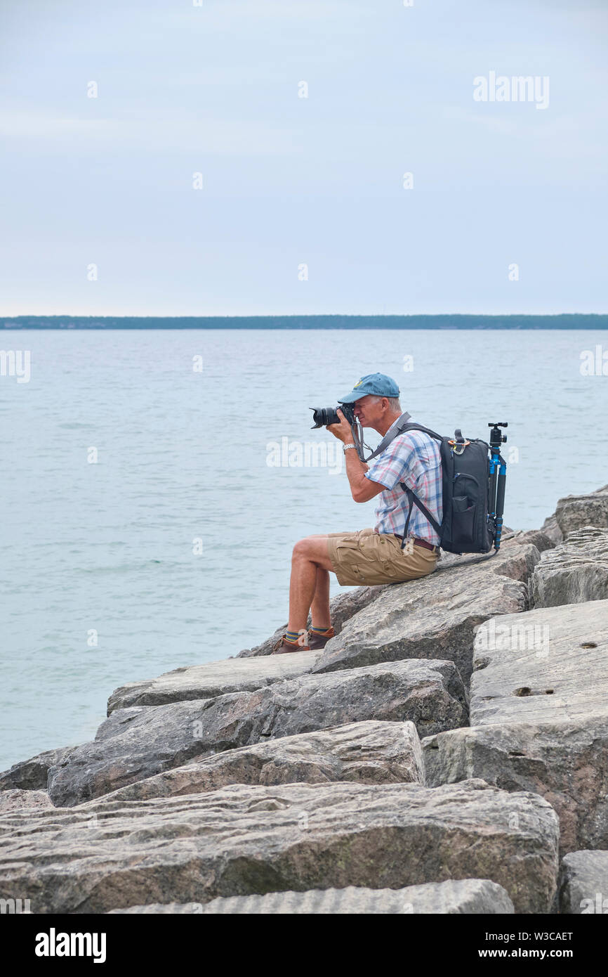 Photographer taking photos while sitting on rocks on the shore of the lake in summer. Stock Photo