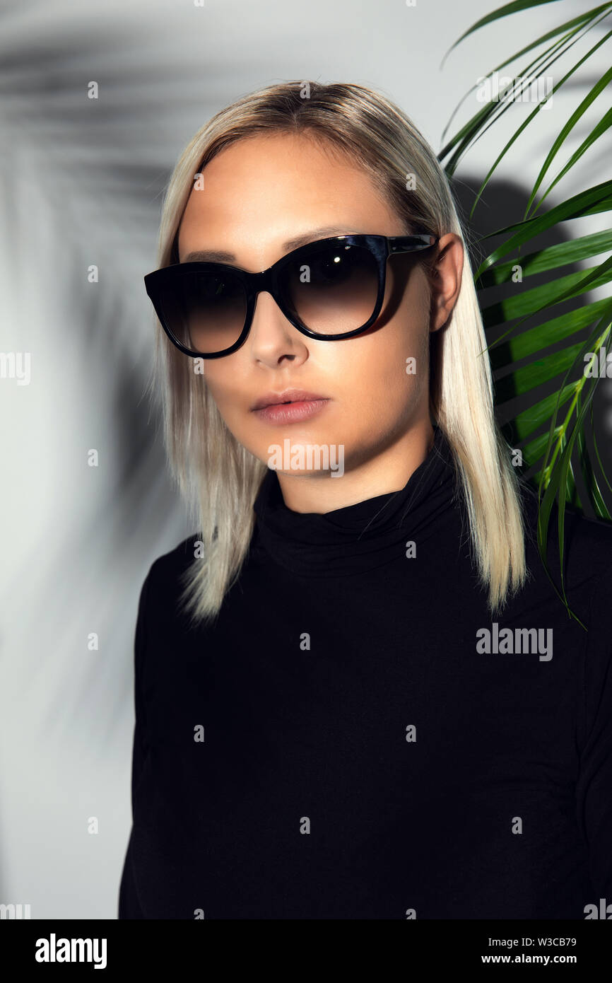 Close-up of woman with sunglasses hiding behind tropical palm leaves Stock Photo