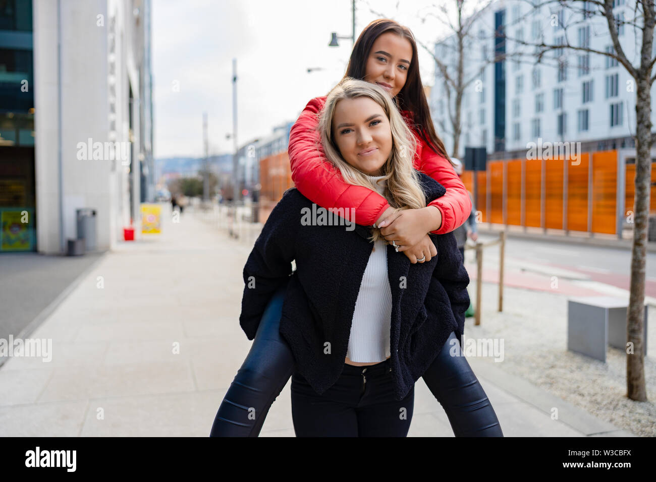 Smiling Female Friends Having Fun and Piggybacking In City Environment Stock Photo