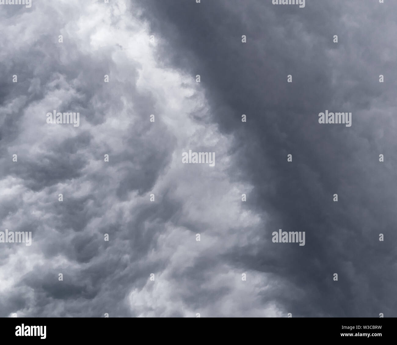 Waves of dark and white storm clouds clash in the sky creating a dramatic abstract image. Stock Photo