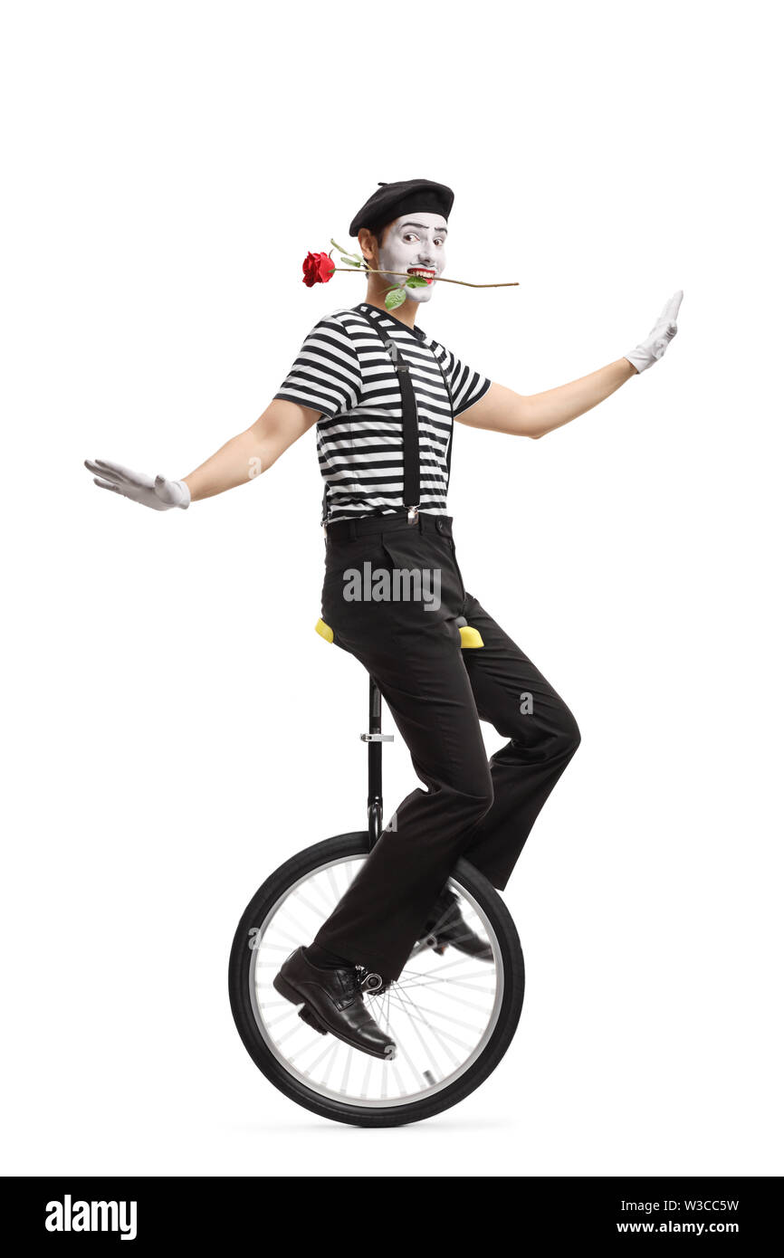 Full length shot of a mime riding a unicycle with a red rose in his mouth isolated on white background Stock Photo