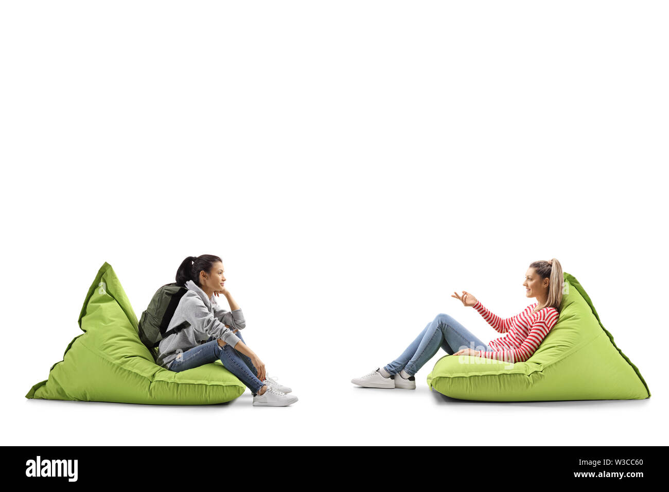 Full length profile shot of two female students sitting on bean bags and  talking isolated on white background Stock Photo - Alamy