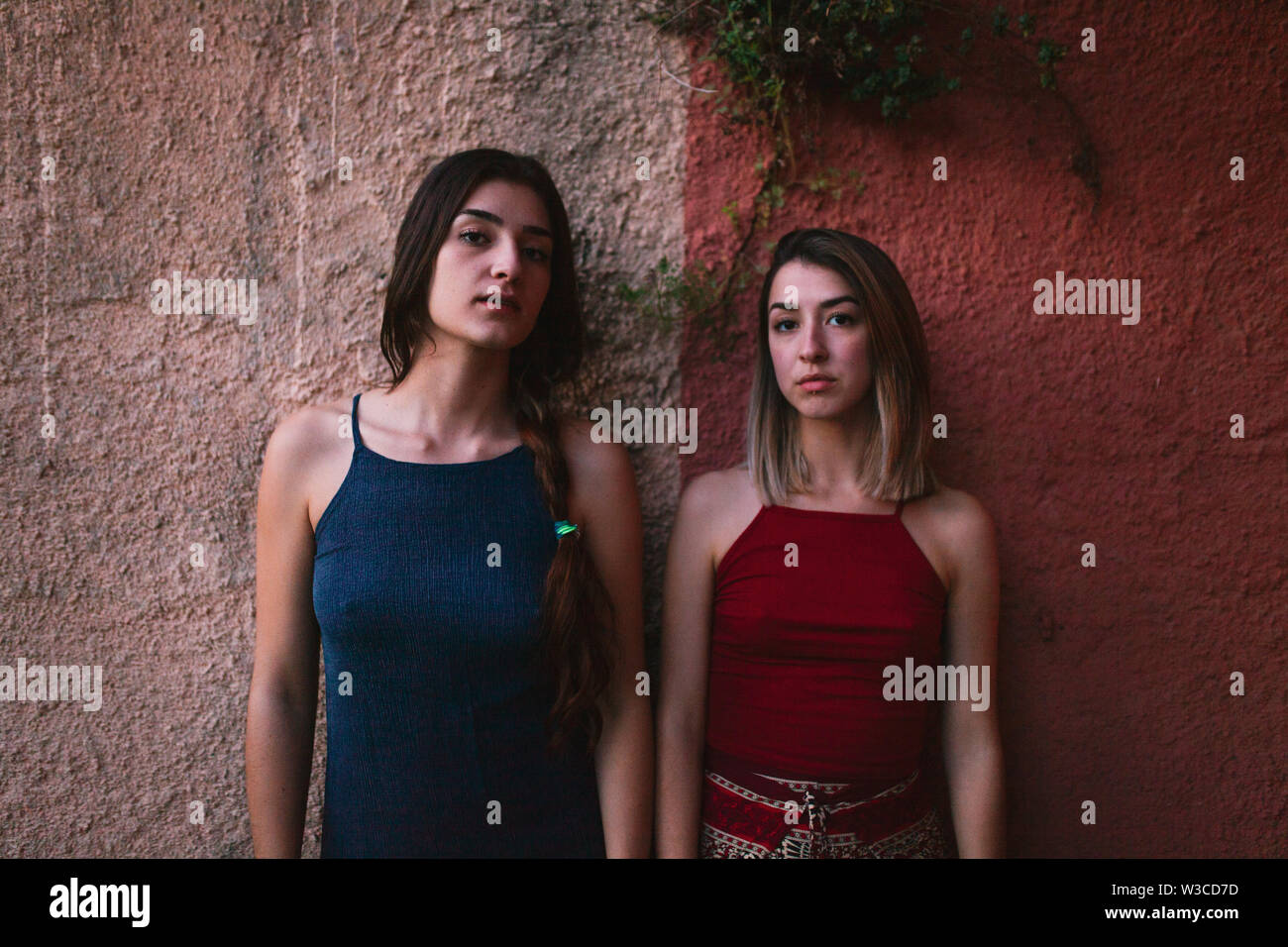 Two young caucasian women watch the sunset from two colors wall Stock Photo
