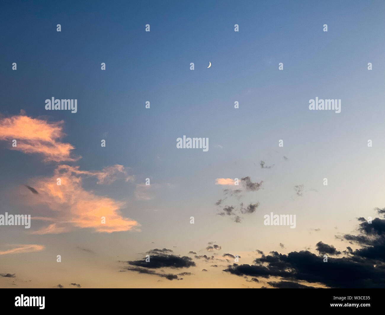 Calm evening sky with moon and dark and pink stratocummulus clouds Stock Photo